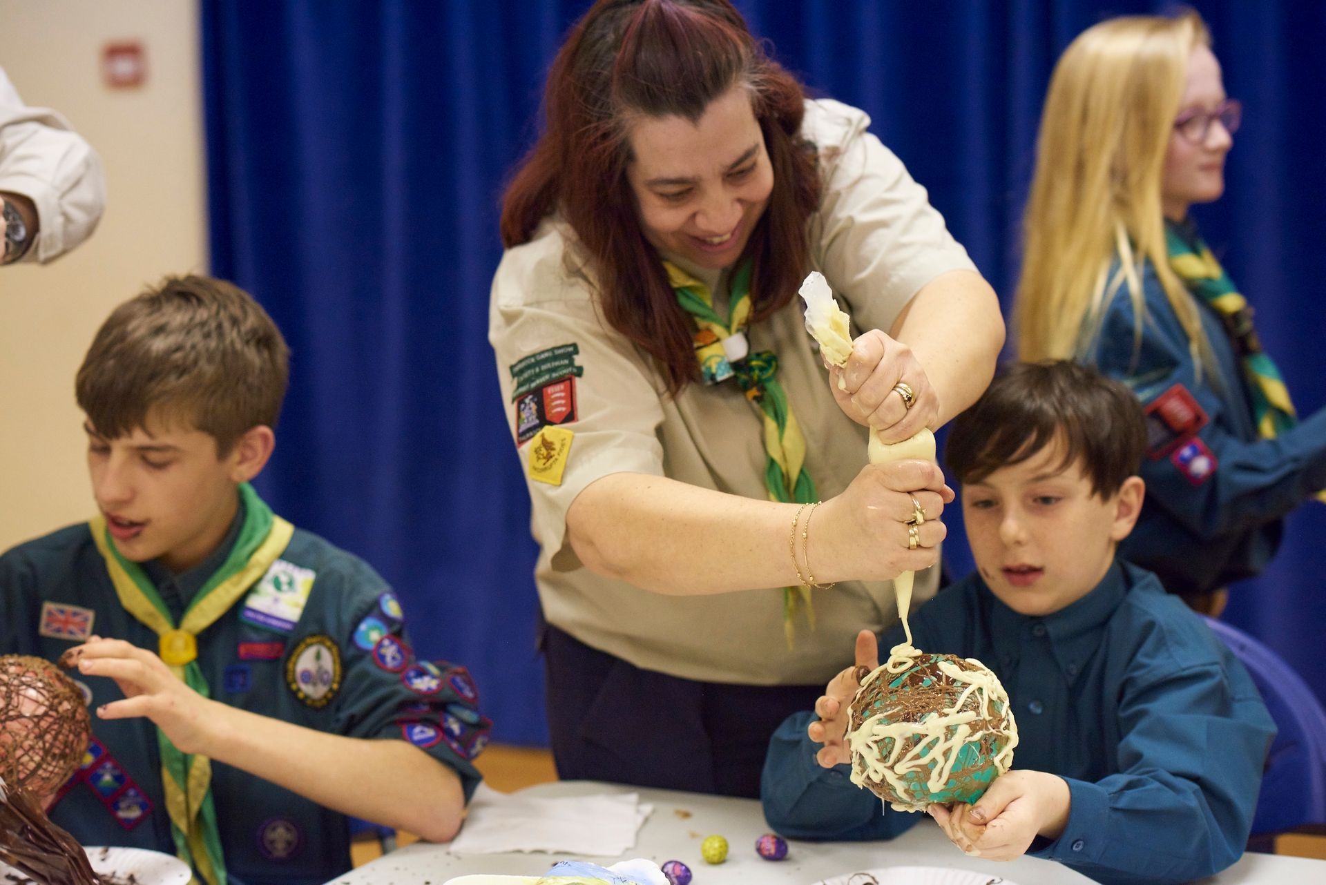 A girl scout helps a boy scout decorate a cake