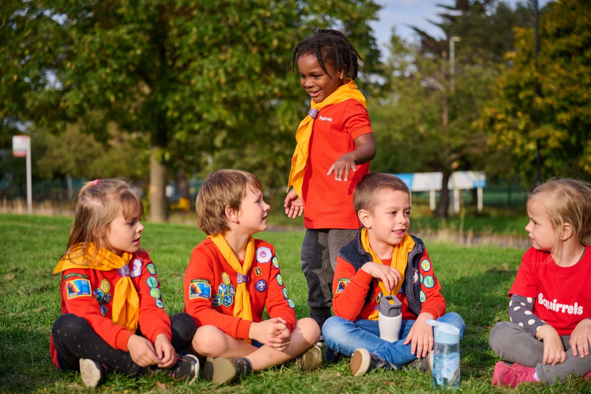 A group of young children are sitting on the grass in a park.