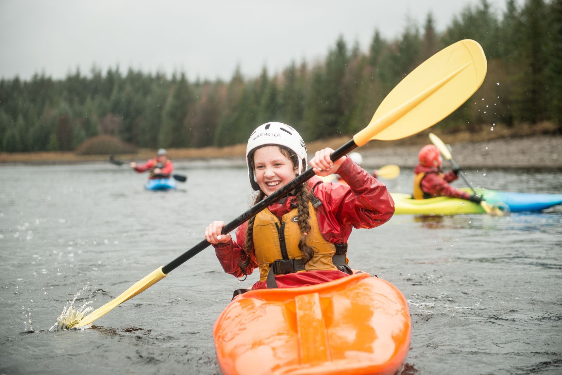 A woman is paddling an orange kayak on a lake.