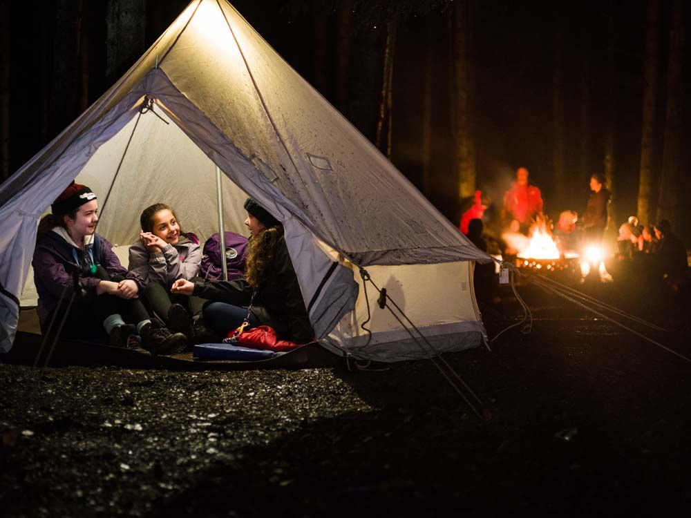 A group of people are sitting in a tent near a fire.