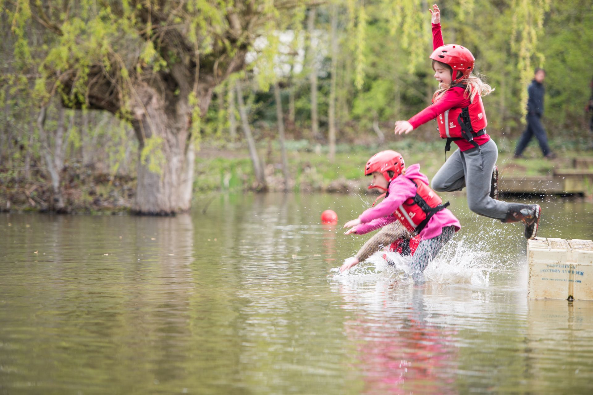 Two young girls are jumping into a lake.