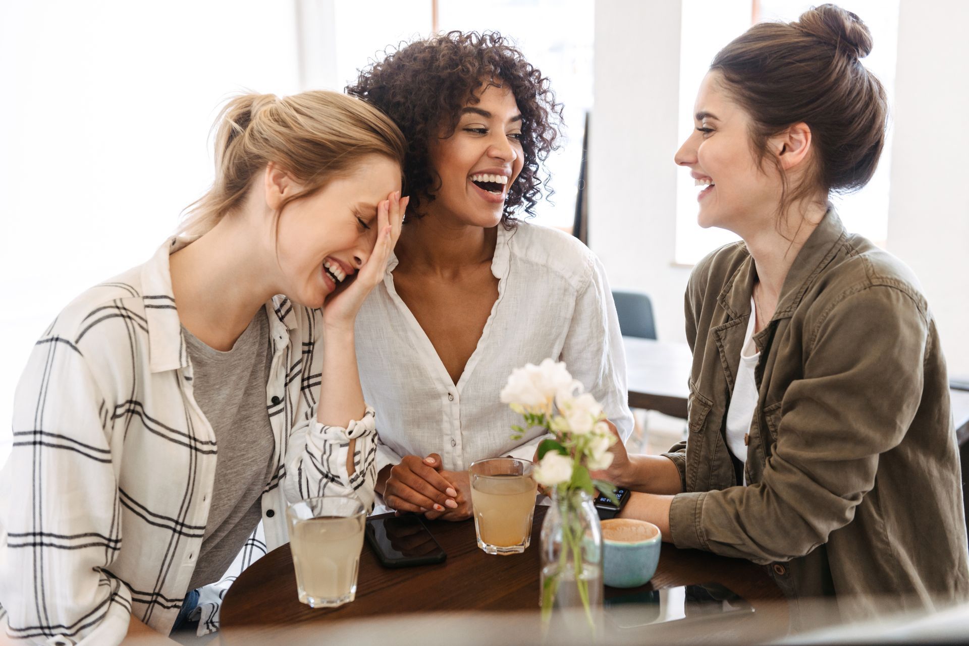 Three women are sitting at a table with drinks and laughing.