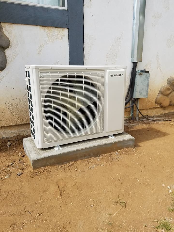 White outdoor air conditioning compressor unit mounted on a concrete slab against a light-colored exterior house wall.