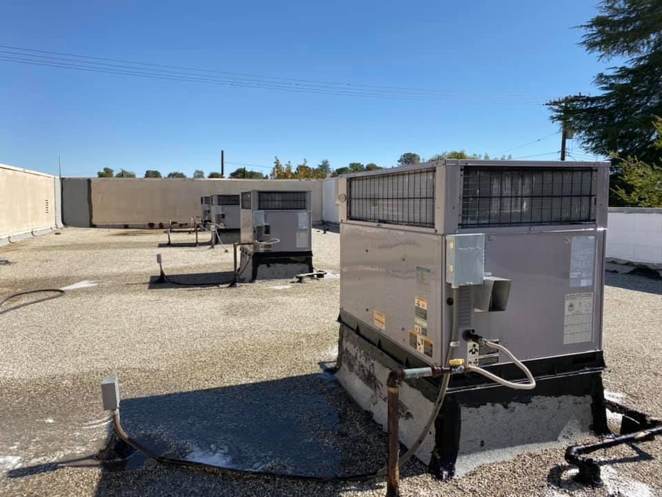 Several HVAC units sit on a gravel-covered flat roof under a clear blue sky.