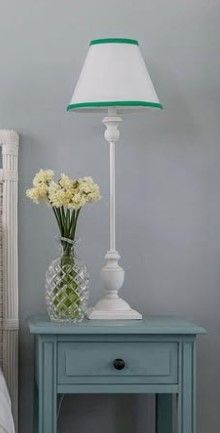 A lamp is sitting on a nightstand next to a vase of flowers.