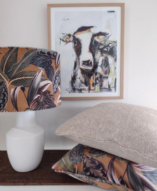 A picture of a cow is above a lamp and pillows