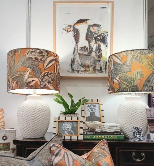 Two lamps are sitting on a nightstand with a picture on the wall above them