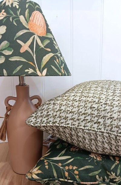 A lamp with a green floral shade is sitting next to a stack of pillows.