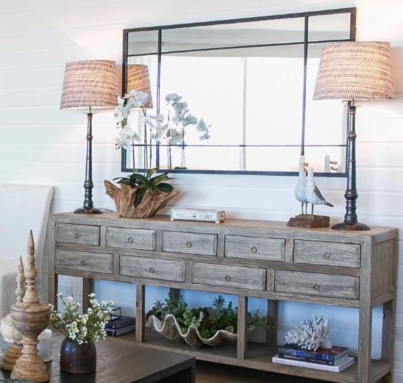 A living room with a dresser lamps and a mirror