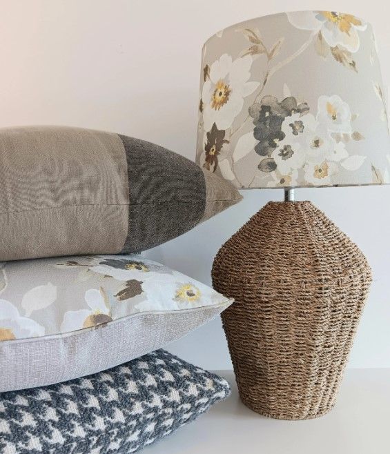 A lamp with a floral shade sits next to a stack of pillows