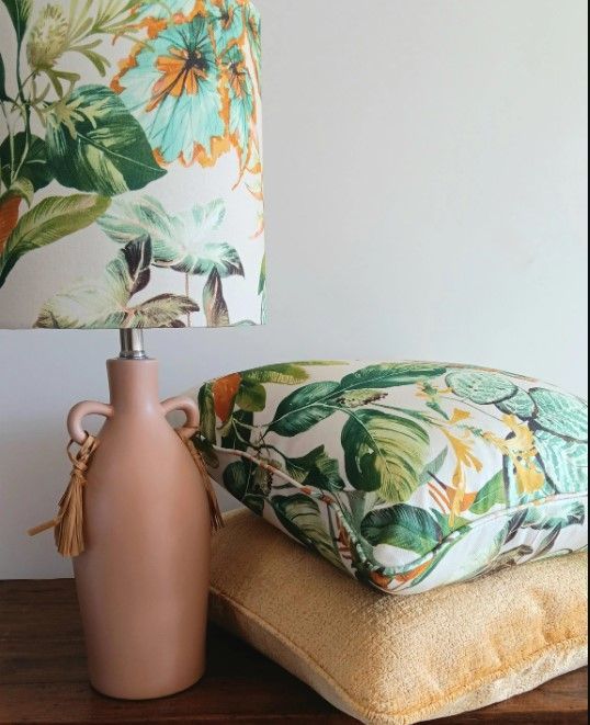 A lamp with a floral shade sits next to a stack of pillows