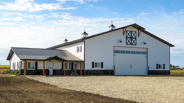 A large white barn with a garage door is next to a house.