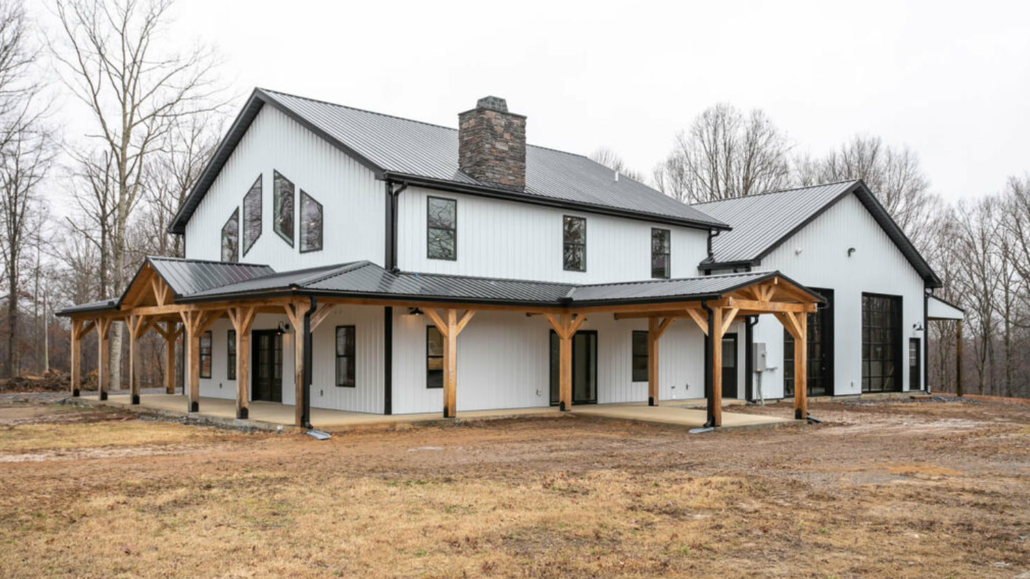 A large white house with a gray roof is sitting in the middle of a field.