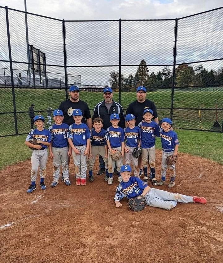 Youth baseball team posing on a field in blue uniforms, with coaches and one player lying in front.