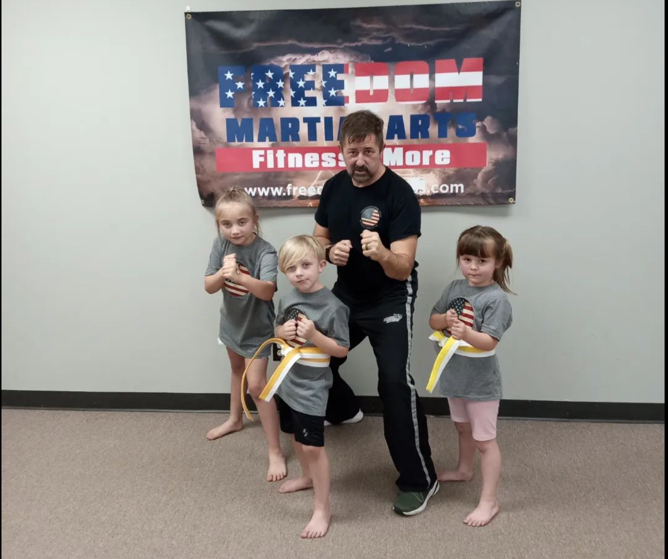 a man and three children pose in front of a martial arts banner