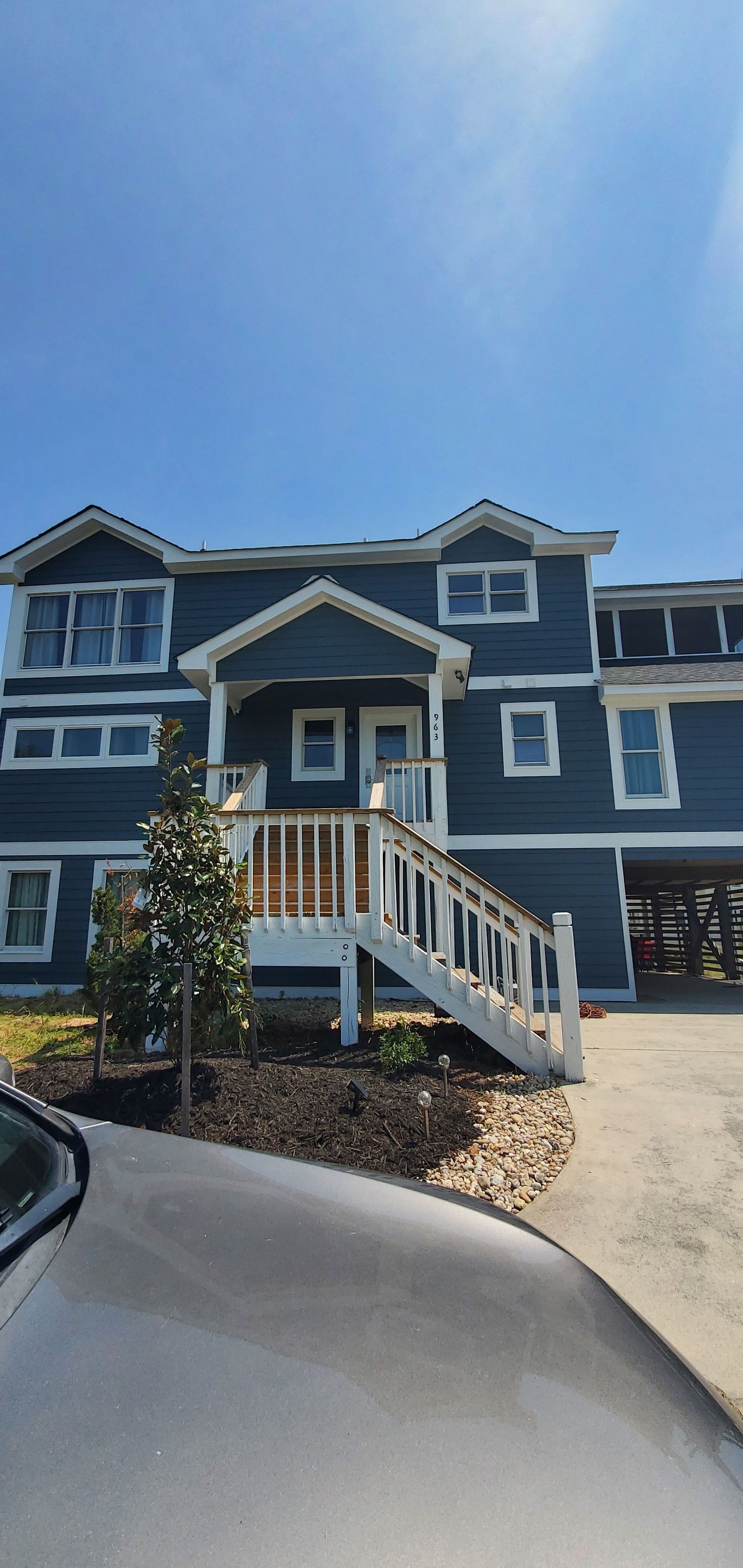 Blue apartment building with white trim and front staircase under a clear sky