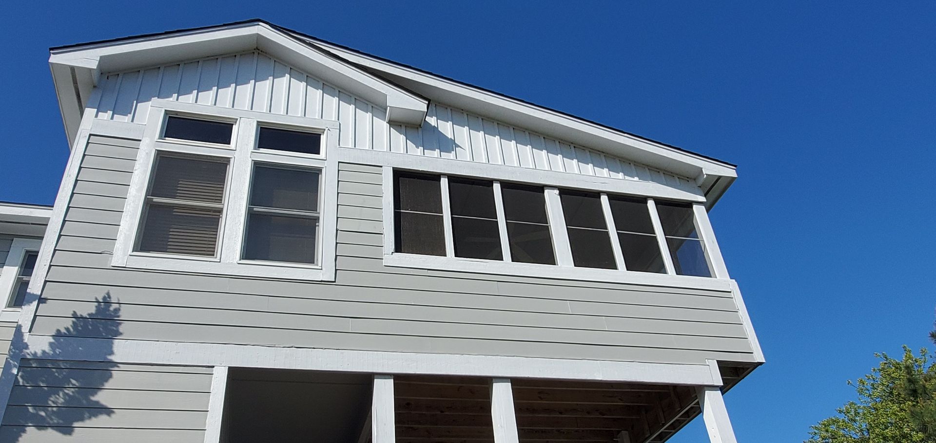 White house facade with gray siding and large windows against a clear blue sky