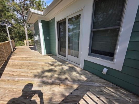 Wooden deck outside a green house with sliding glass doors and windows, viewed along a fenced side yard