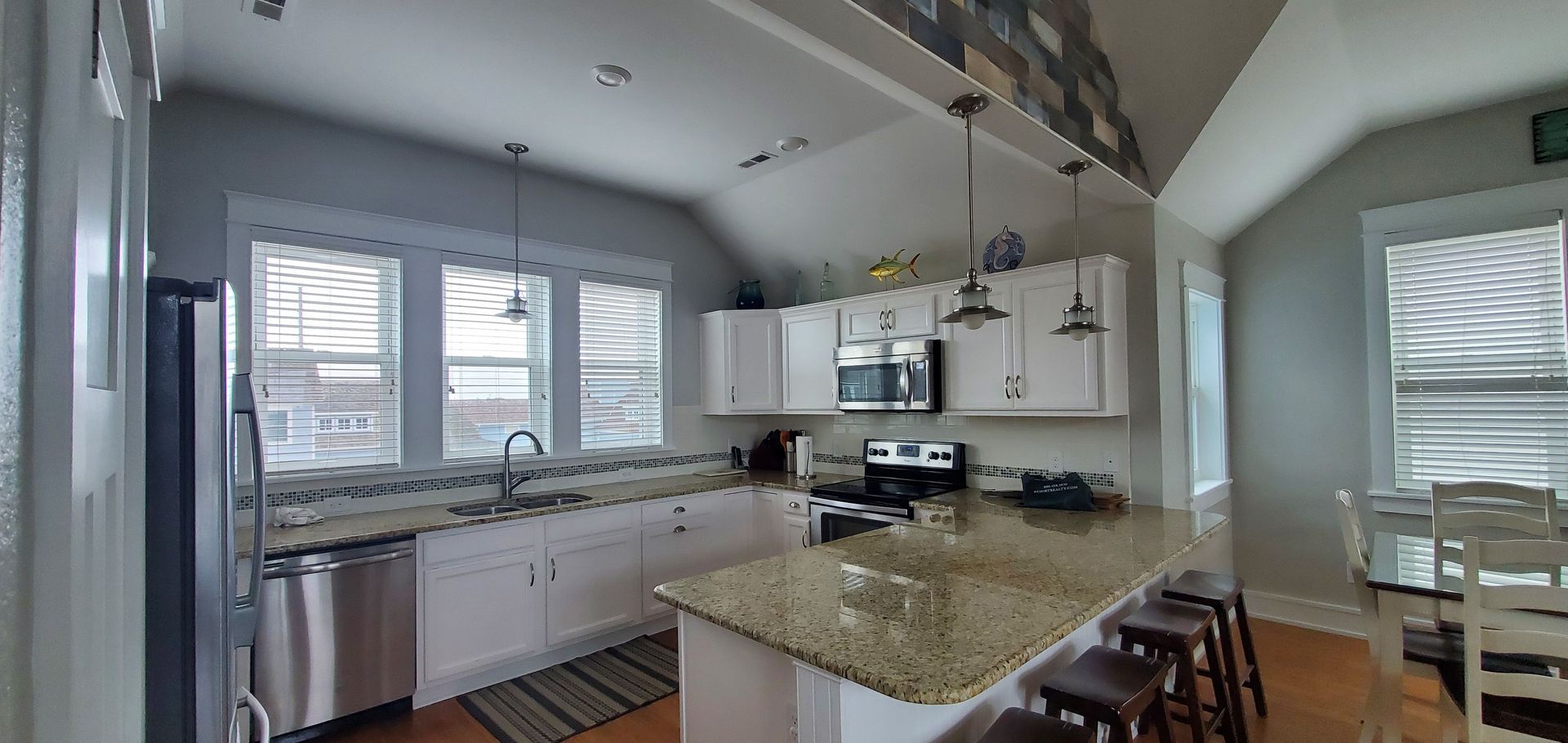 Bright kitchen with granite island, white cabinets, stainless appliances, and windows with blinds