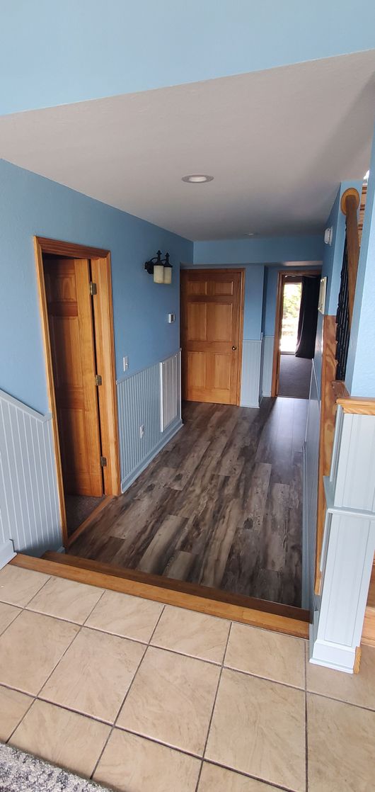 Hallway with blue walls, wood doors, tiled entry, and dark wood flooring leading to a doorway.