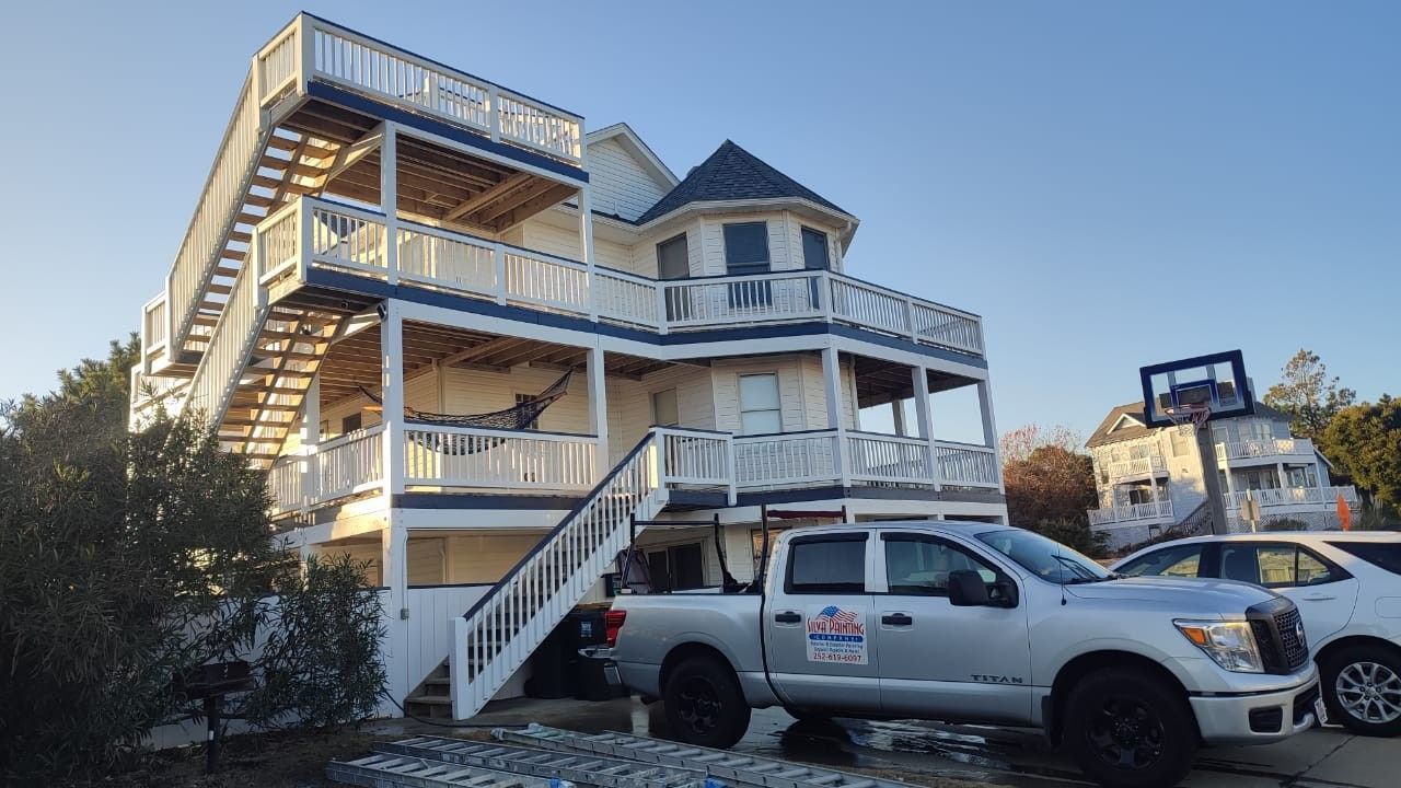 White beach house with stairs and balconies beside parked vehicles in daylight