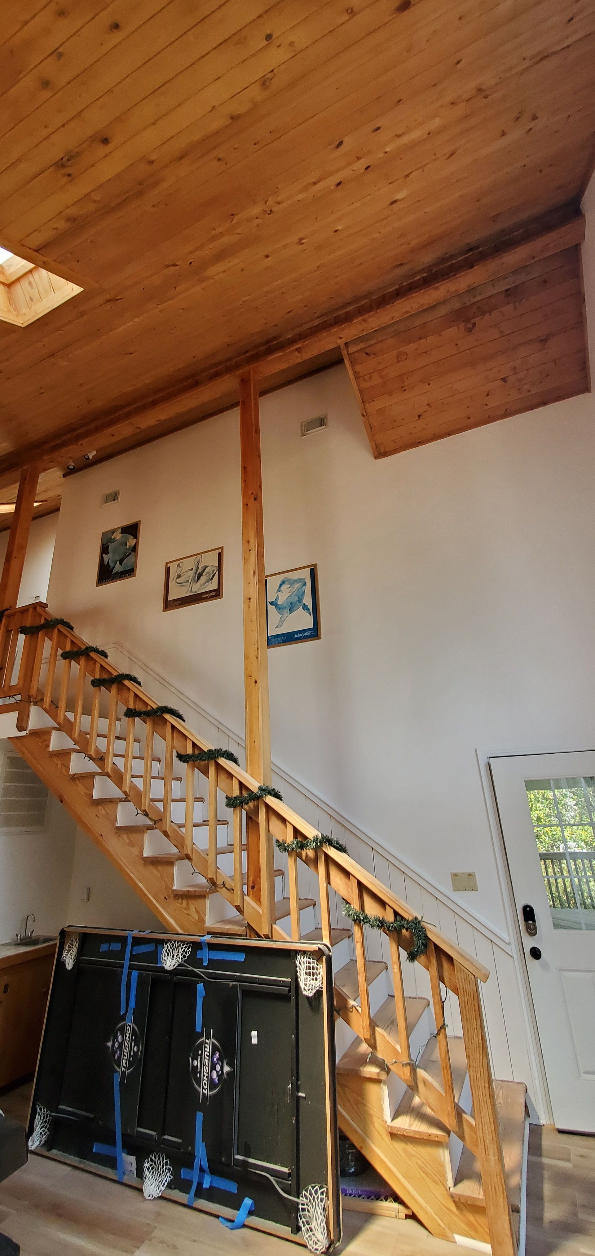 Wooden staircase with railing under a slanted wood ceiling in a loft-style room.