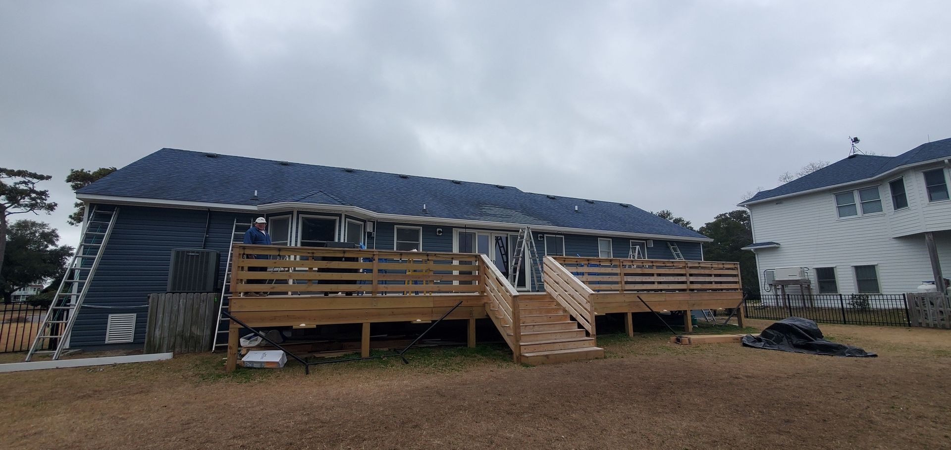 Mobile home with blue roof and wooden porch in a gravel lot, with another house beside it.