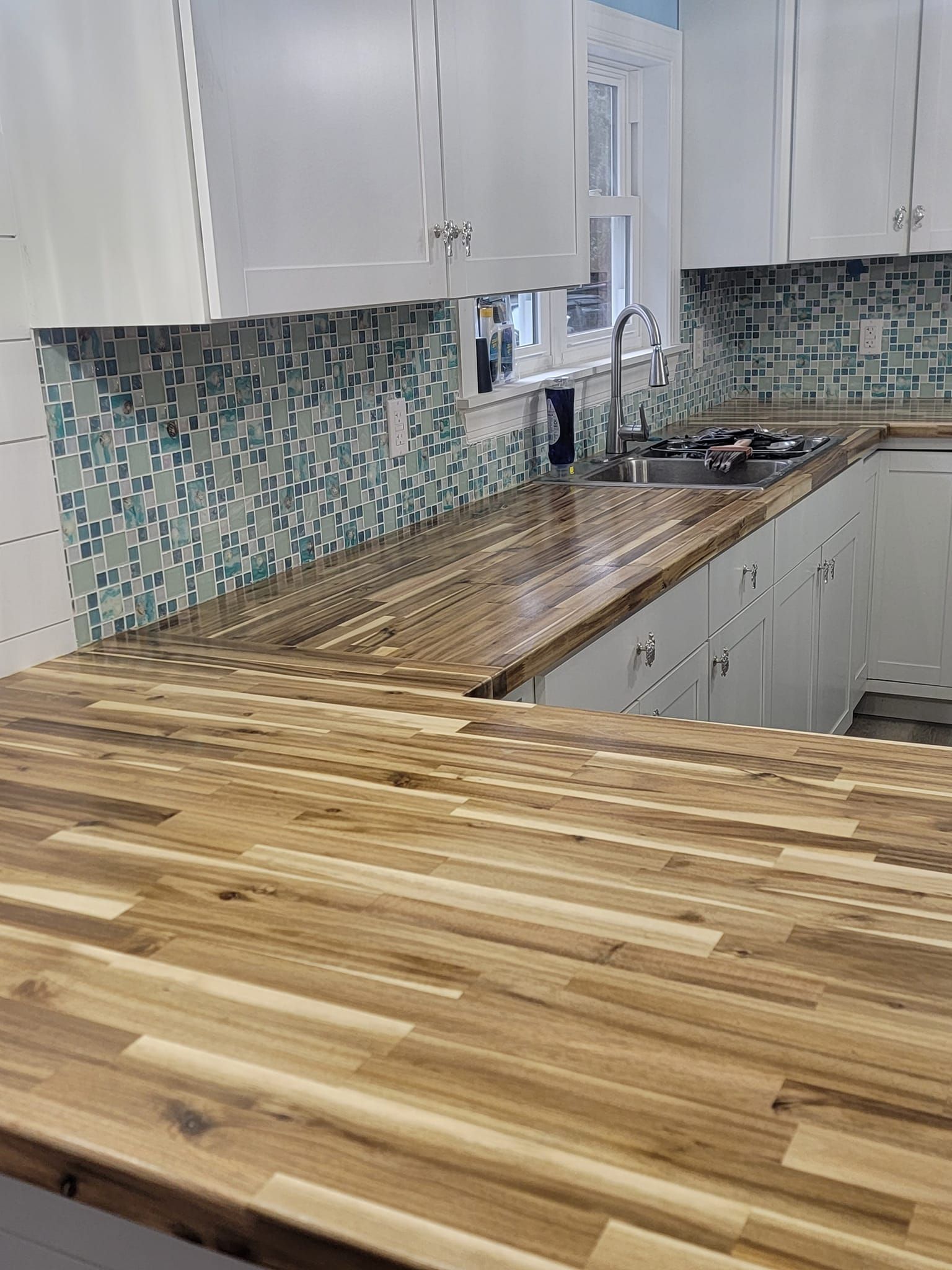 Modern kitchen with white cabinets, mosaic tile backsplash, and butcher-block countertops.
