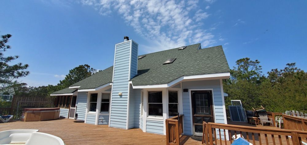 White house with blue shutters and a tall chimney, viewed from a wooden deck under a clear blue sky