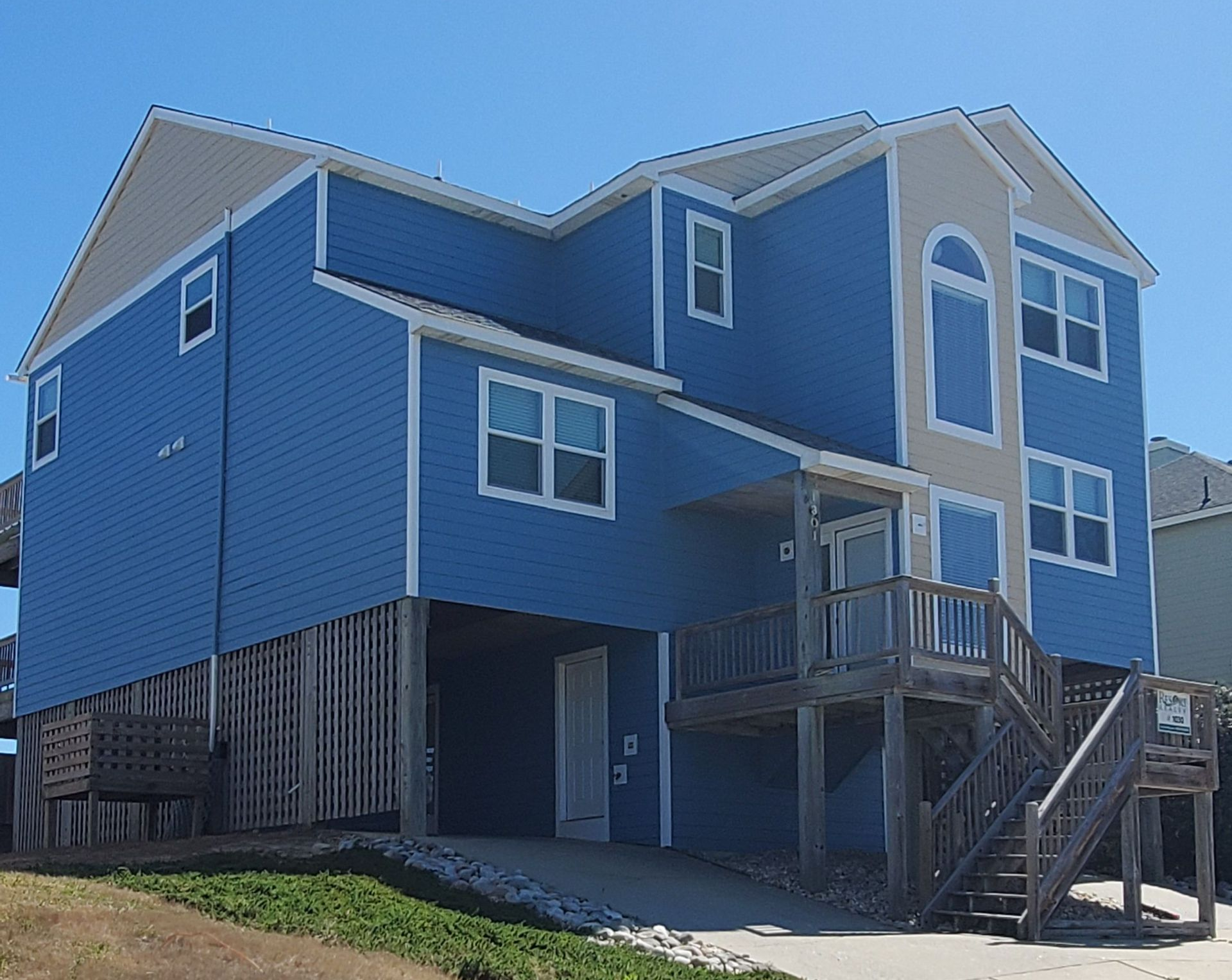 Blue two-story house with white trim and raised porch, viewed from the side on a sunny day