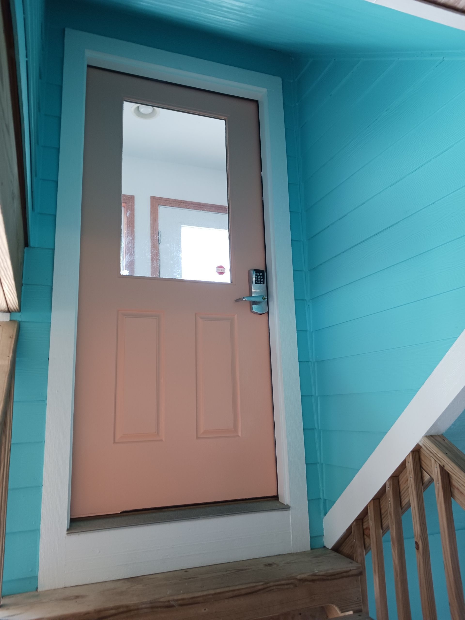 Pink door with window in a turquoise exterior wall, next to a stair railing.