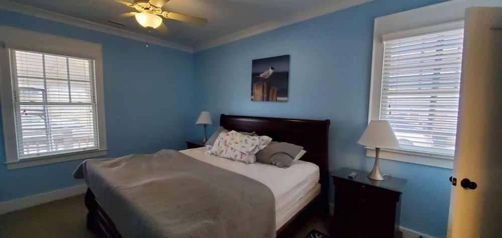 Blue bedroom with a bed, nightstands, lamps, and windows with white blinds