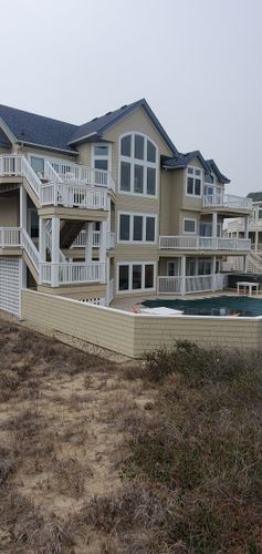 Multi-story coastal condo with white balconies and beige siding beside a pool and sand dunes