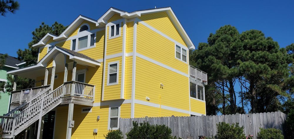 Bright yellow house with white trim, balconies, and stairs under a blue sky