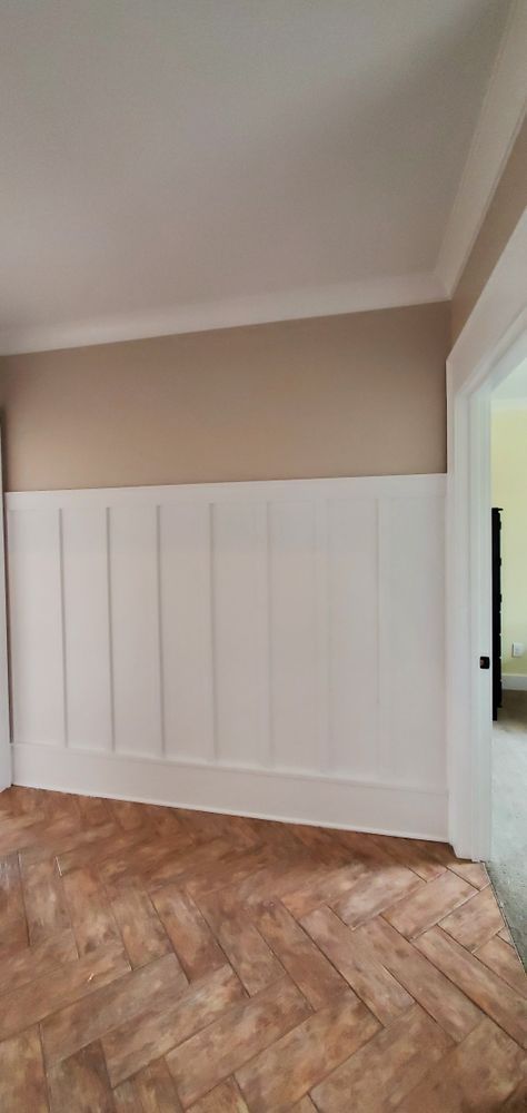 Empty room with white wainscoting, beige walls, and a herringbone wood floor