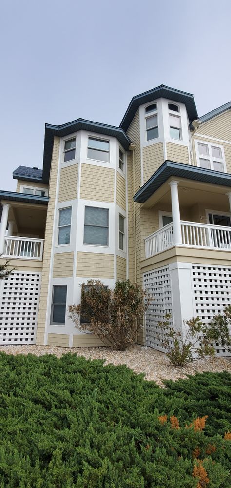 Townhouses with white siding and beige trim behind green shrubs on a cloudy day