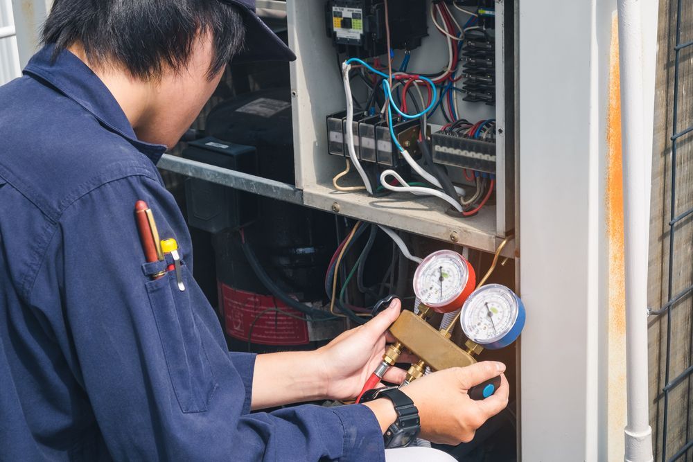 A Man In A Blue Shirt Is Working On An Air Conditioner — Coastal Gasfitting & Plumbing In Mount ST John, QLD