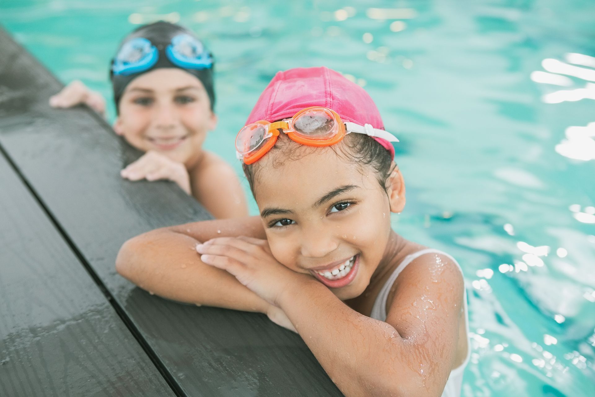 Two young girls are leaning on the edge of a swimming pool.