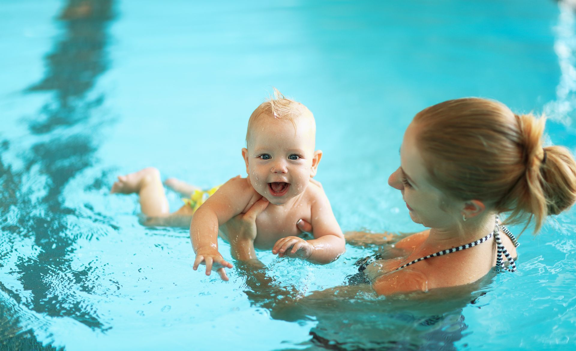 A woman is holding a baby in a swimming pool.