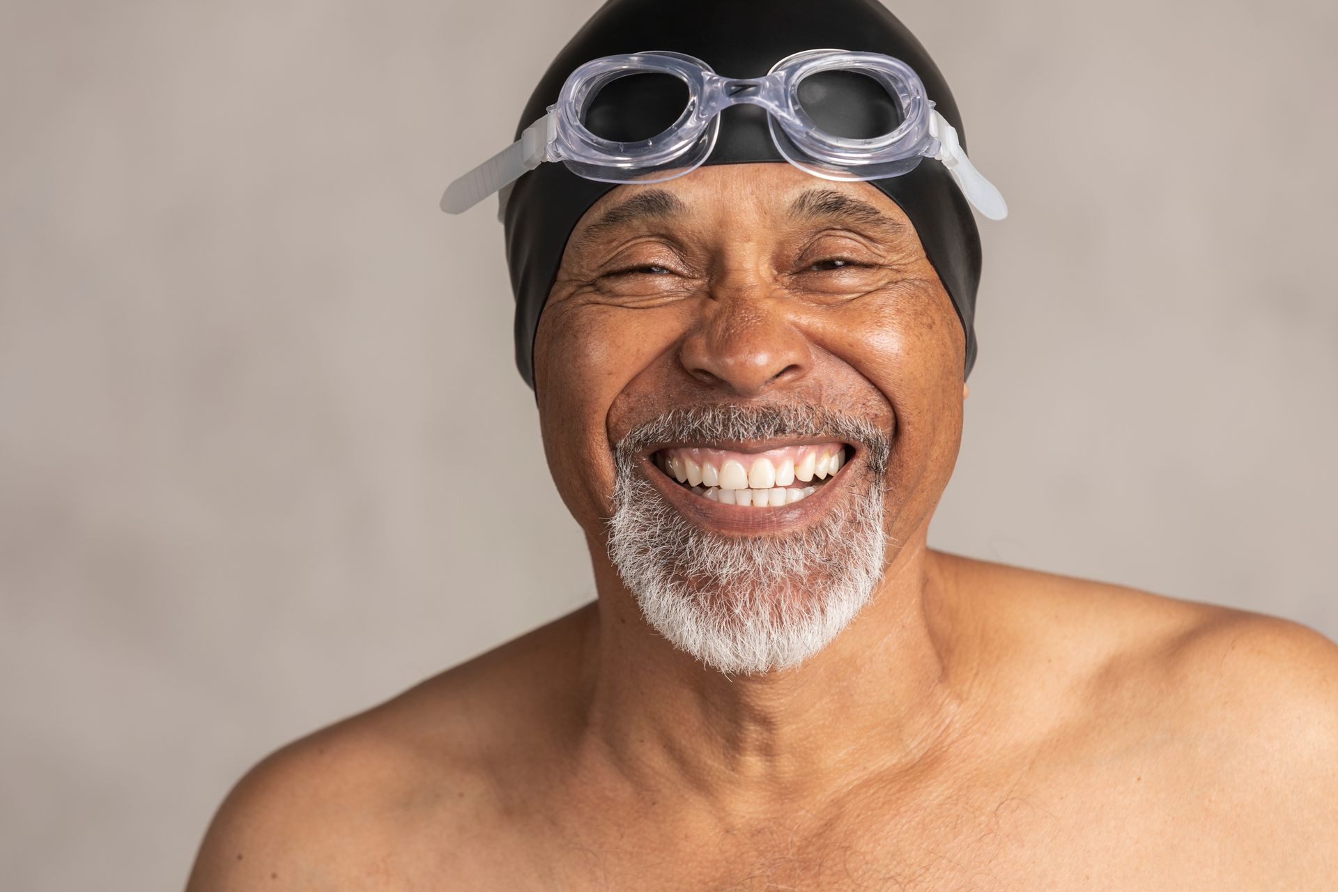 An older man wearing a swim cap and goggles is smiling.