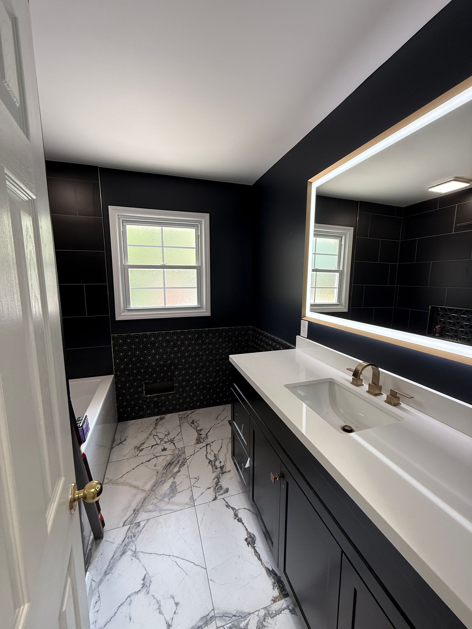Modern bathroom with black walls, white marble floor, vanity, sink, mirror, and window.