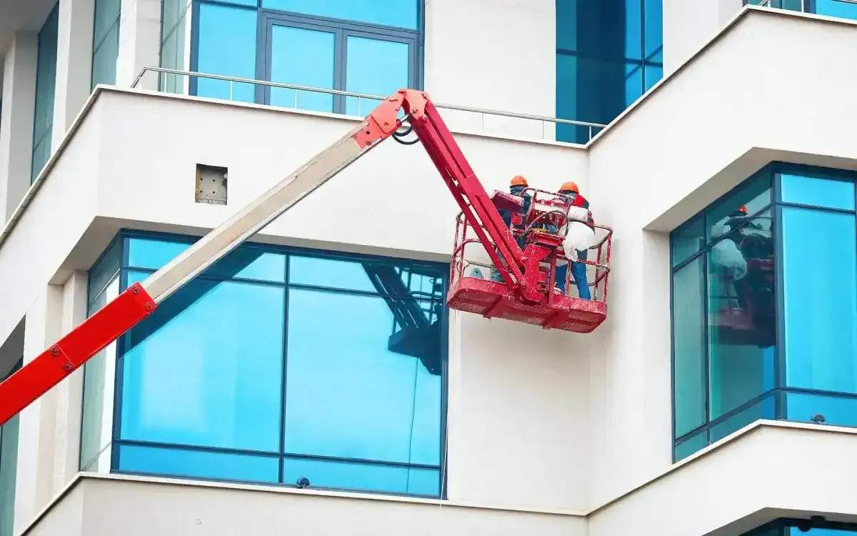 Workers in a red lift cleaning blue-tinted windows on a white building