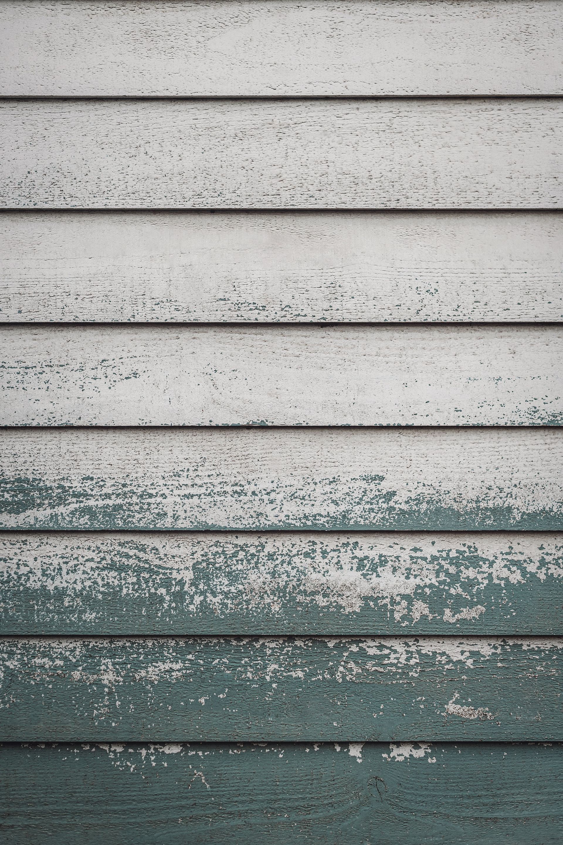Weathered gray and teal horizontal wooden siding with peeling paint
