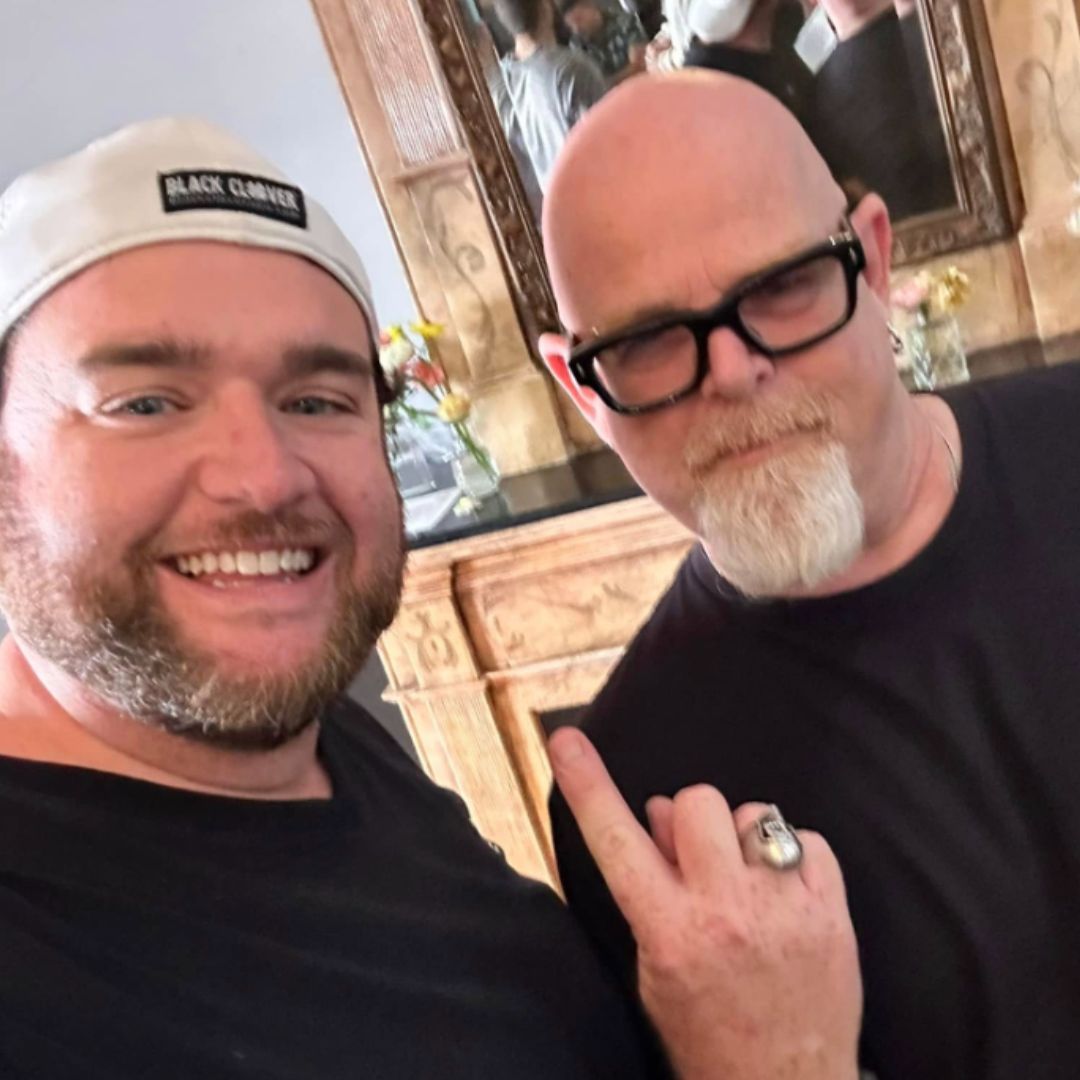Two men posing for a picture with one wearing a hat that says black camden