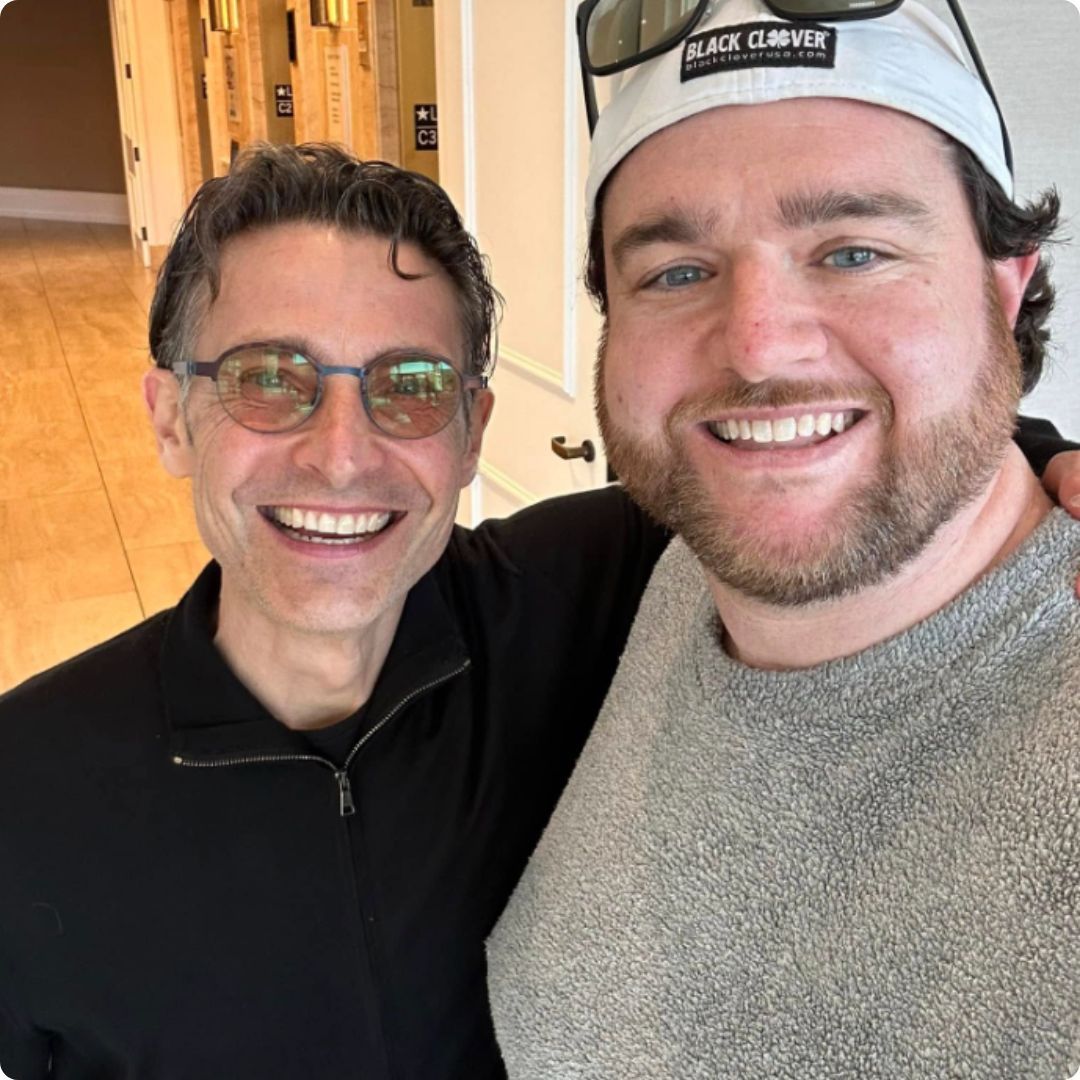 Two men posing for a picture with one wearing a hat that says black clover