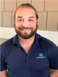 A man with a beard is wearing a blue polo shirt and smiling.