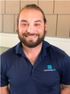 A man with a beard is wearing a blue polo shirt and smiling.