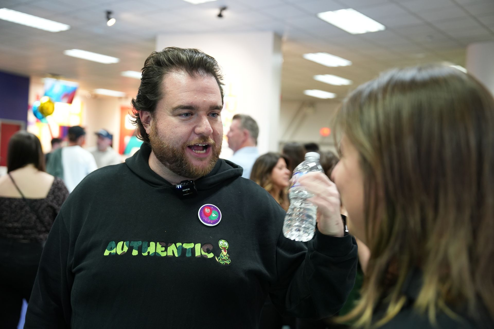 A man wearing a hoodie that says atlantic is talking to a woman holding a bottle of water.