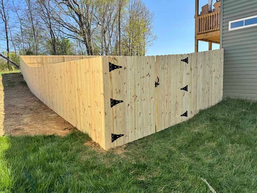 Wooden fence with black hinges, surrounding a grassy area next to a house.