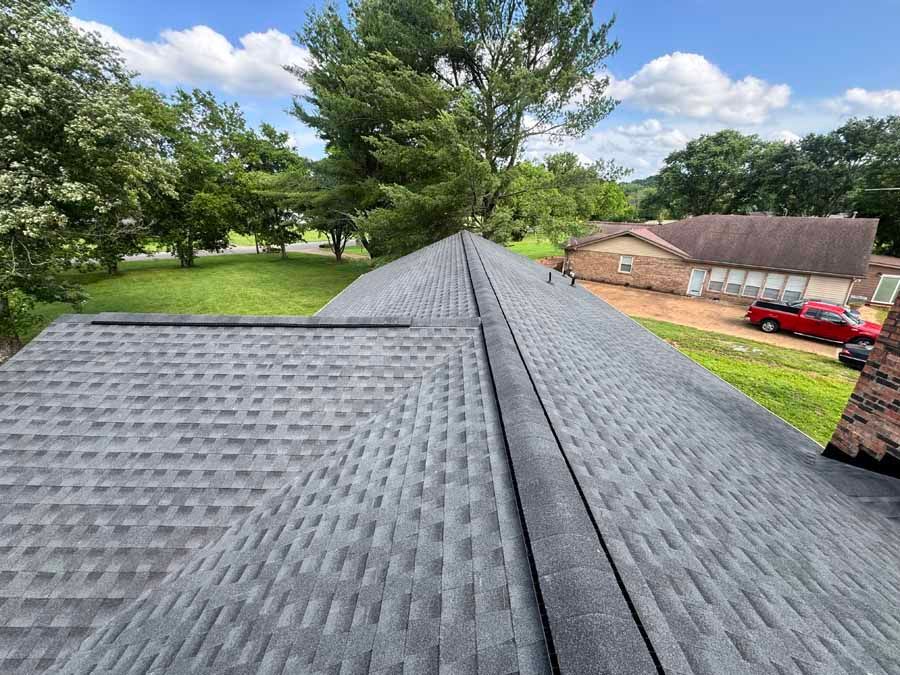 Gray shingle roof on a house with green trees and grass in the background.